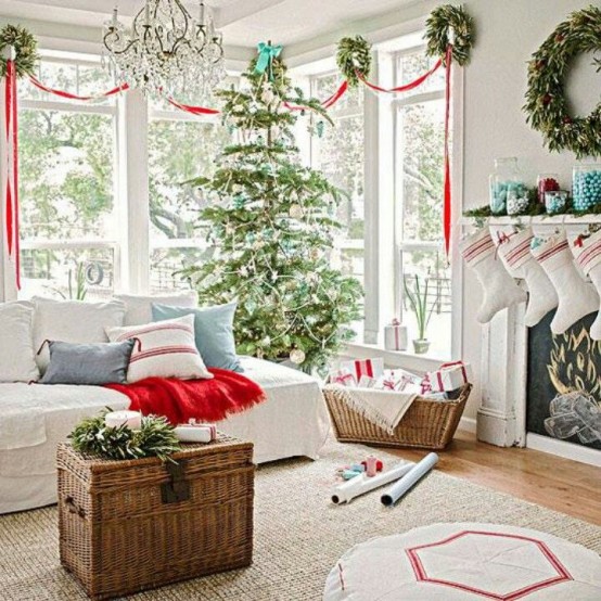 a lovely and chic Christmas living room with a Christmas tree decorated in blue and silverm with green wreaths and red ribbons plus some holiday pillows