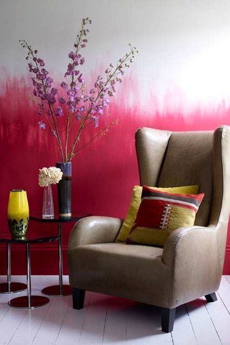 a bold space with an ombre fuchsia wall, a taupe wingback chair and a side table with bloomign branches is wow