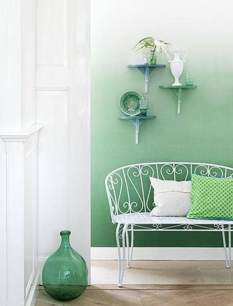 an ethereal entryway with an ombre green wall, a white metal bench, green pillows, shelves with various vases and decor is a stylish idea