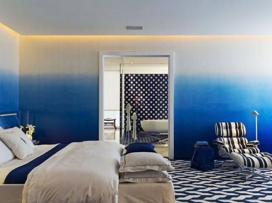 a bold bedroom with ombre blue walls, white furniture, navy and white bedding and a bold printed rug on the floor is wow