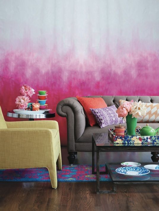 a bold living room with an ombre fuchsia wall, a grey tufted sofa, a yellow chair,a  bold rug and lots of colorful pillows and bright tableware