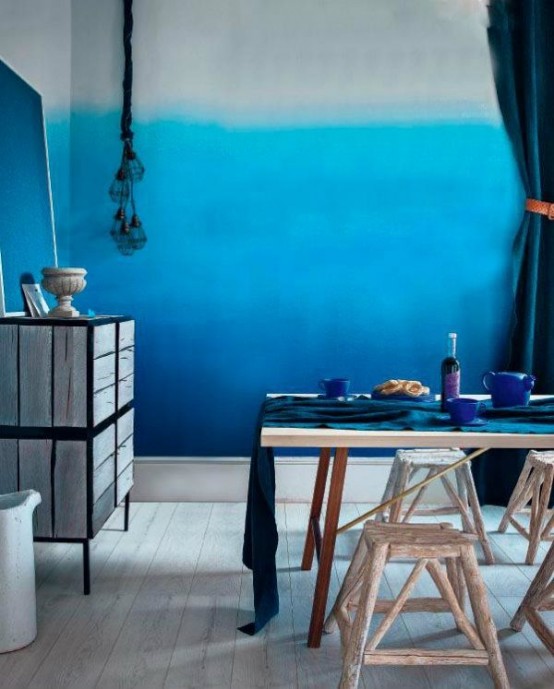 a pretty dining room with statement ombre blue walls, a dining table and chairs and stools plus a sideboard, some blue decor and tableware