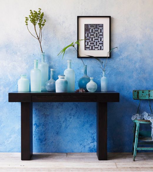 a bold ombre blue accent wall, a black console table with an arrangement of light blue vases and a black and white artwork is a stylish space