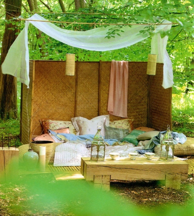 a bright outdoor sleeping space with a low bed with pastel and printed pillows, a space divider around the space, a low table and a canopy is a lovely relaxing space