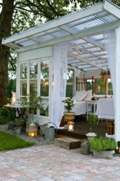 a white ex-glasshouse turned into a garden bedroom with elegant shabby chic furniture, lots of greenery and candle lanterns around