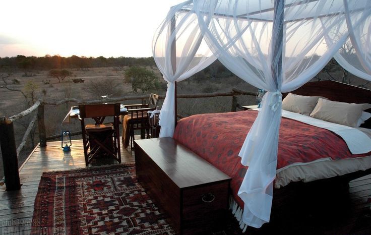 a boho outdoor bedroom with a canopy bed with neutral bedding, a desk and a chair and a rug for more coziness