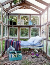 a former glass house with a metal bed and bright bedding, a blue suitcase and artwork and potted plants