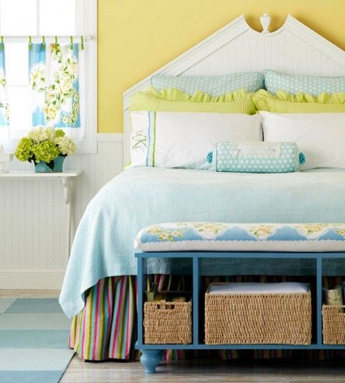 a cheerful farmhouse spring bedroom with a white bed, blue and yellow bedding, a blue bench, bold yellow blooms