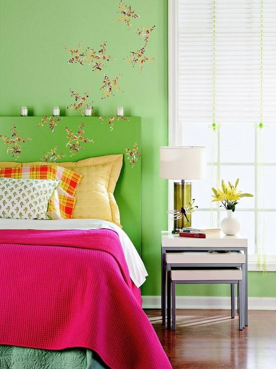 a bright spring bedroom with green walls, a green bed with colorful bedding, floral decals and bright blooms in a  vase