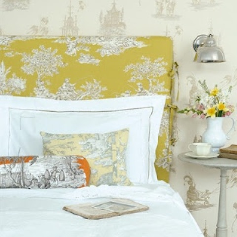 a bright spring bedroom with printed wallpaper, a printed headboard and linens, a vintage sconce and bold blooms
