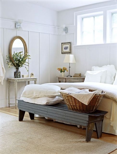 a neutral farmhouse bedroom with vintage rustic furniture, neutral bedding, elegant lamps and mirrors and some greenery in a vase