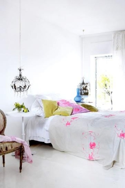 an eclectic bedroom in whie, with cheerful pink and green bedding, crystal chandeliers and a vintage chair