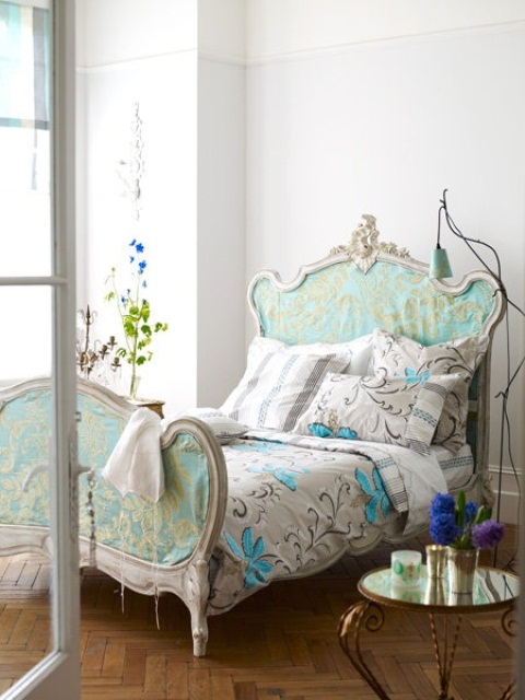 a refined bedroom with a chic vintage bed in blue, with floral bedding, lamps, blooms and candles