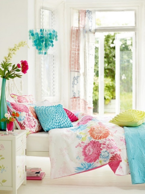 a bright and colorful spring bedroom with white furniture, colorful bedding, seashell chandelier and potted blooms and greenery