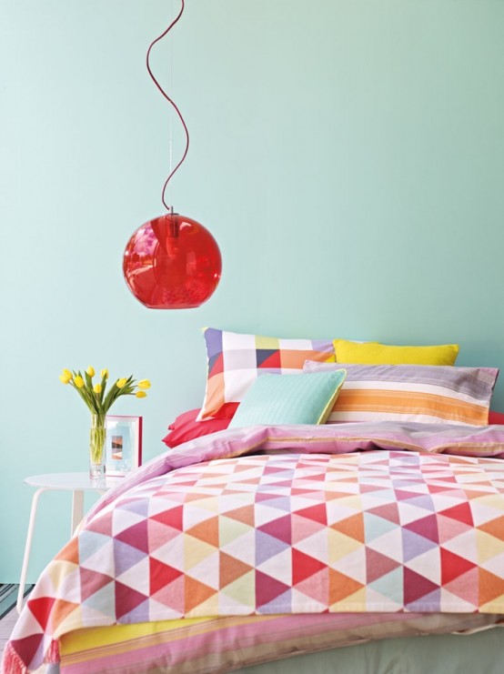 a colorful spring bedroom with blue walls, a bed with colorful bedding, a red pendant lamp and bold blooms in a vase