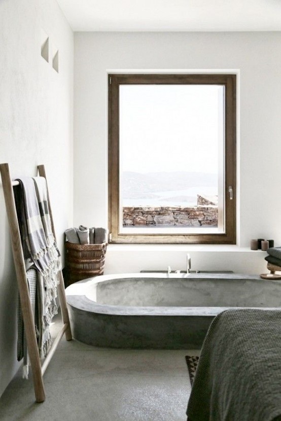 a minimalist bathroom with concrete and stone, with a sunken concrete bathtub, a view to the sea