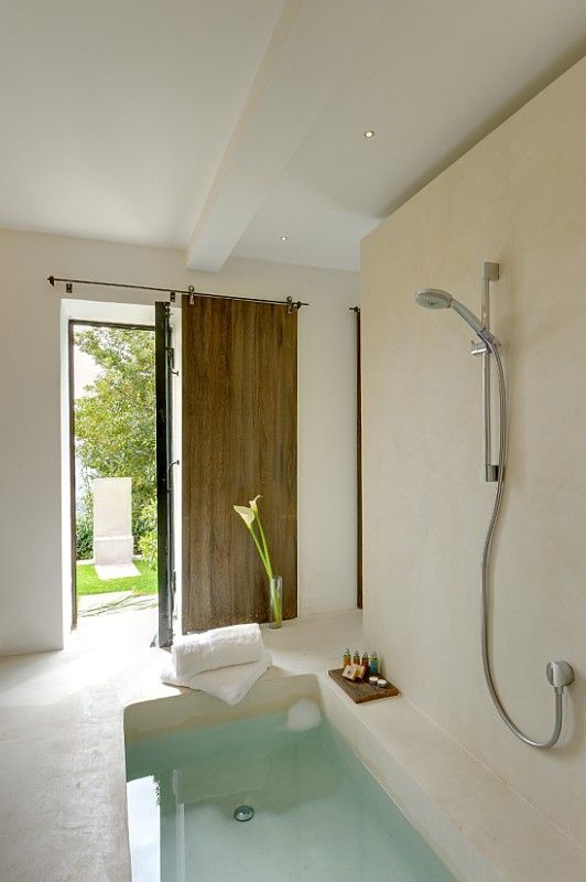 a simple and nautral bathroom in concrete and stone, with a sunken bathtub and a sliding door for a breath of fresh air