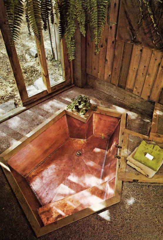a natural bathroom with a stone floor, pallet wood walls and an asymmetrical bathtub clad with copper inside it
