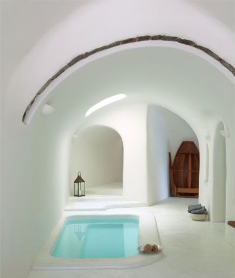 a minimal white bathroom with an arched ceiling plus a sunken bathtub, lanterns and sponges around