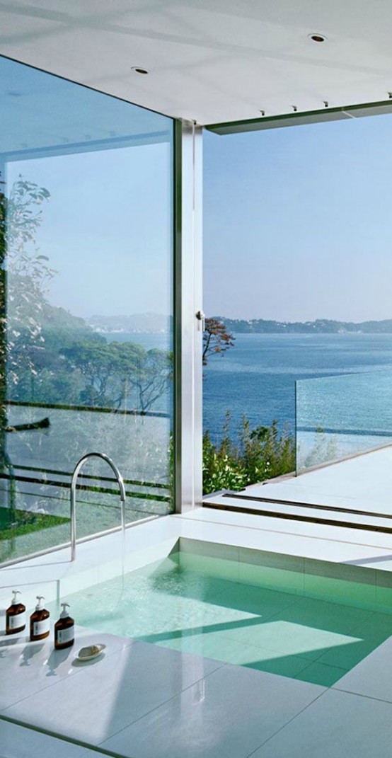 a minimalist bathroom all glazed, with a view, with sunshine and air, with a sunken bathtub that takes maximum of these views