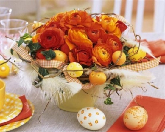 a bright Easter centerpiece with citrus and red and orange flowers, feathers and checked ribbons