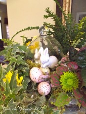 a lush spring centerpiece with lots of greenery, blooms and fake bunnies and pink eggs