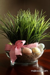 a glass bowl with hay, grass and eggs plus a pink ribbon is a fresh Easter decoration