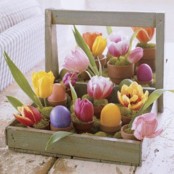 a crate with moss and colorful blooms, eggs and greenery in pots for Easter decor