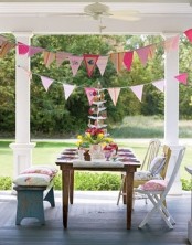 a bright Easter table set on the front porch, colorful buntings, colorful porcelain and pillows on the chairs
