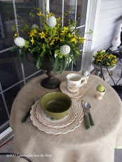 a table styled on the front porch with a greenery and floral arrangement with eggs, some colorful eggs and porcelain