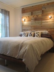 a rustic industrial bedroom with a rough wood accent wall, a wood and metal bed with neutral bedding and wall sconces