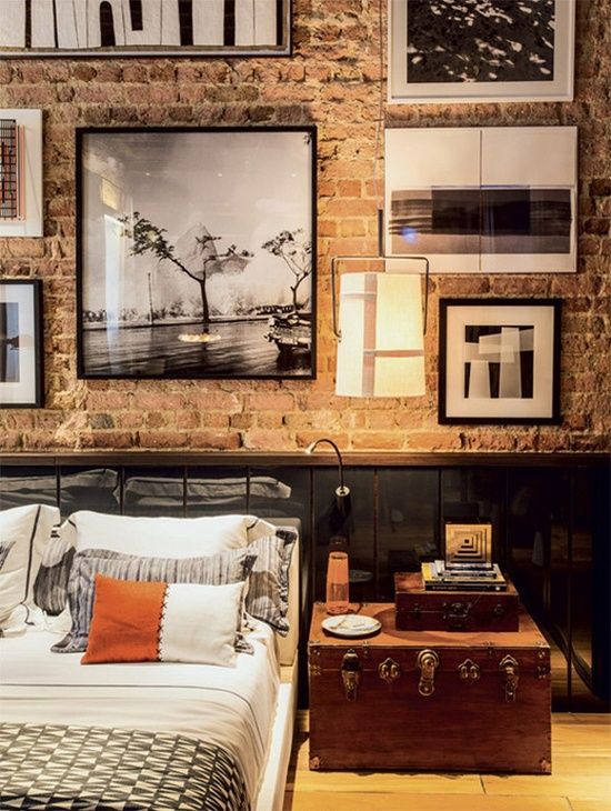 an industrial bedroom with brick walls, black paneling, a black metal bed, a chest as a nightstand and a large black and white gallery wall