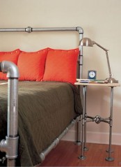 a shiny metal bed with grey and coral bedding, a piping nightstand and a metal table lamp is a cool space