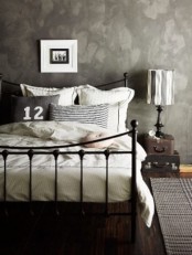 a moody bedroom with a black metal bed with neutral bedding, stacked suitcases and a table lamp is a relaxing space