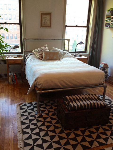 a boho meets industrial bedroom with a metal bed, neutral bedding, a printed rug, stained nightstands and metal lamps, potted plants