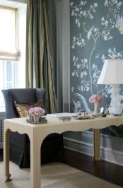 a romantic feminine home office with a blue floral accent wall, a beautiful carved desk and a a grey chair plus a refined table lamp