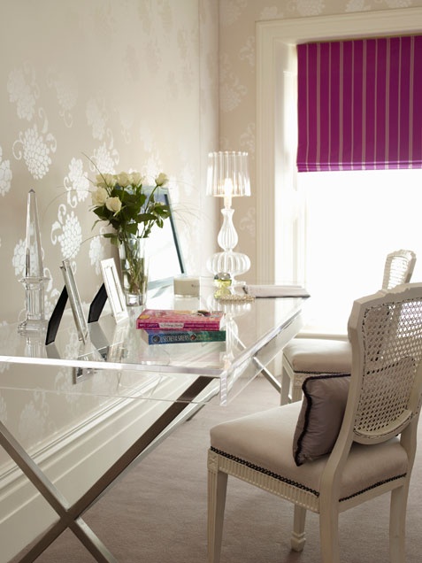a stylish feminine home office with neutral printed wallpaper, a glass desk, a refined chair and a purple Roman shade