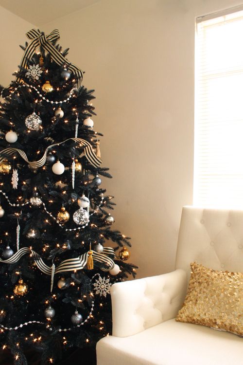 a chic and refined black Christmas tree with lights, black, gold and white ornaments and snowflakes and beads