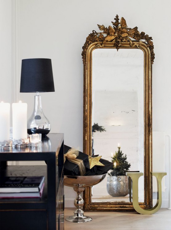 a full height mirror in a refined gilded frame and a stack of black and gold Christmas gifts and a table lamp for lovely and chic decor