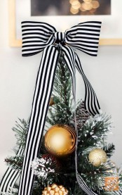 a flocked Christmas tree decorated with gold and silver ornaments, snowy pinecones and a striped black and white bow on top is very elegant and chic