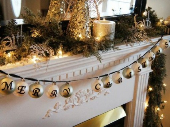 a Christmas mantel decorated with fir branches, gold candles, mini trees and a galrand with ornaments and letters is very lovely