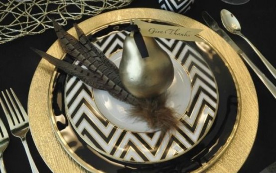 a sophisticated black, white and gold Thanksgiving place setting with a gilded pear and feathers is a very chic and bold idea