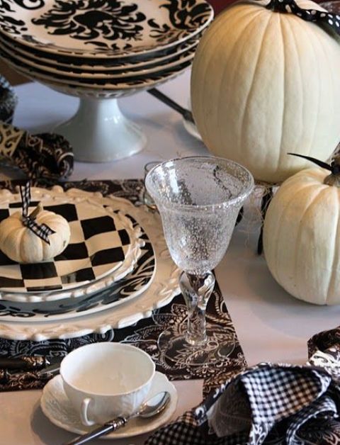 a chic black and white Thanksgiving tablescape with checked plates, white pumpkins and patterned placemats is amazing and very bold