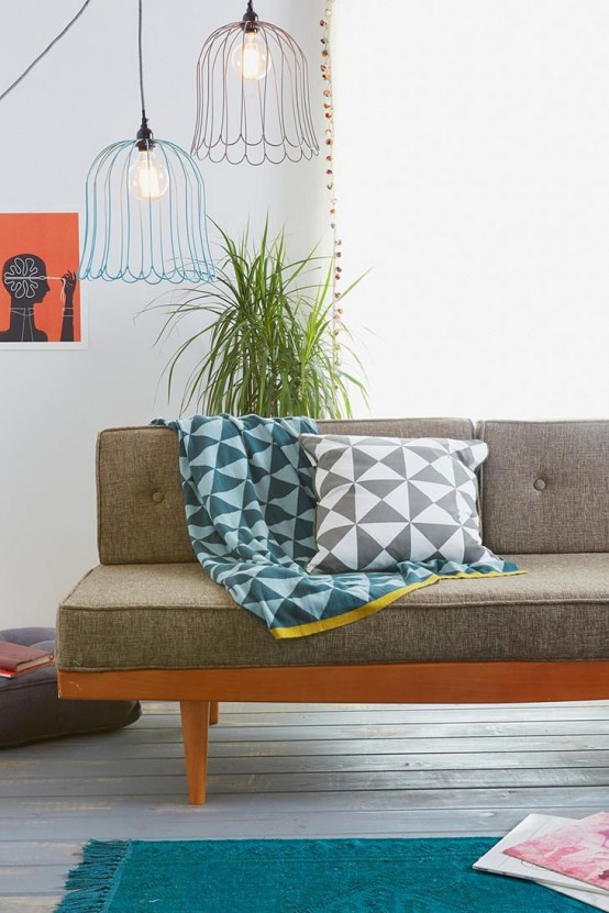 a grey mid-century modern sofa with a stained frame, a blue rug, printed pillows, pendant lamps and a potted plant
