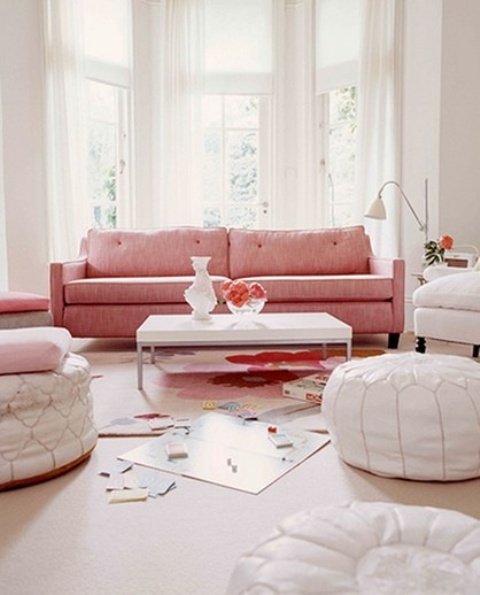 a neutral living room with a bay window, a pink mid-century modern sofa, white Moroccan poufs and a chair plus a coffee table