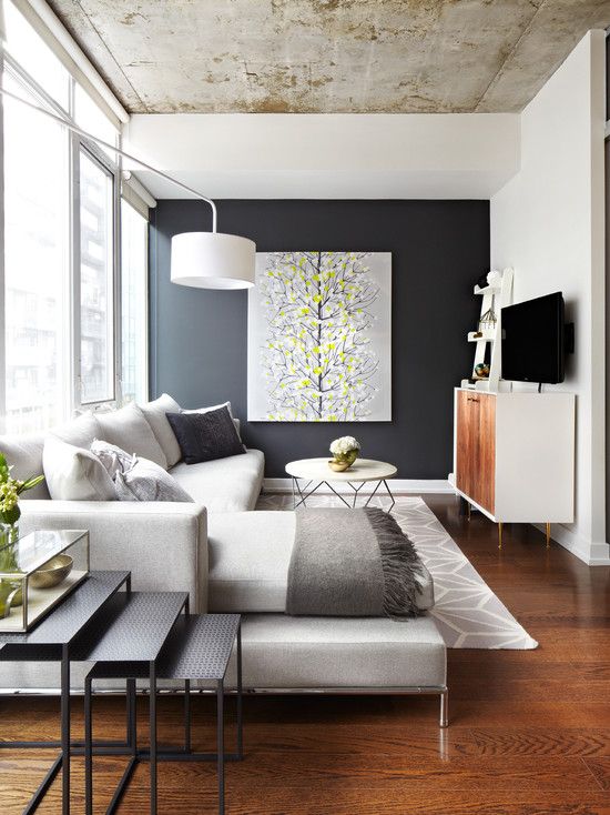 a small contemporary livign room in a monochromatic color scheme, a black accent wall with an artwork, a ceiling of concrete and a stack of tables