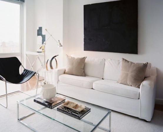 a small contemporary living room in neutrals, with a black artwork and chair, with a glass table and lots of natural light