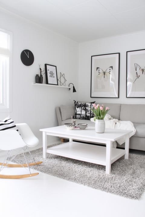 a cozy Scandinavian living room with arworks, comfy furniture, a grey rug and a black clock