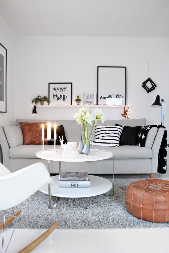 a small Scandinavian living room done in neutrals, with touches of black, printed pillows and string lights and lamps