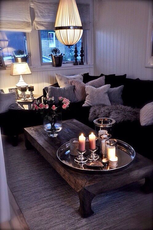 a boho living room all done in neutrals, with a black fur sofa, a crystal chandelier, a wooden table and white fabric shades